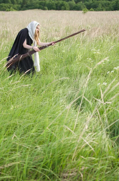 ほうきで魔女が密度の高い草の生い茂った緑のフィールドにさまよう — ストック写真