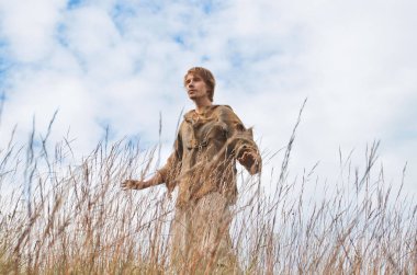 mavi gökyüzü karşı vahşi sararmış kulakları ortasında bir ortaçağ köylü gibi giyinmiş genç adam