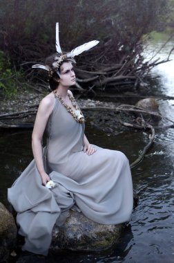 Genç kadın bir Nehri yakınında bir kayanın üzerinde oturur ve suya bir beyaz çiçek float sağlar