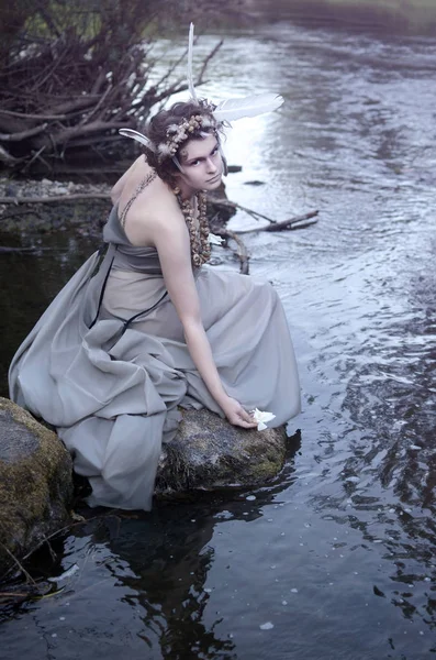 年轻女子坐在河边的岩石上 让一朵白花漂浮在水中 — 图库照片