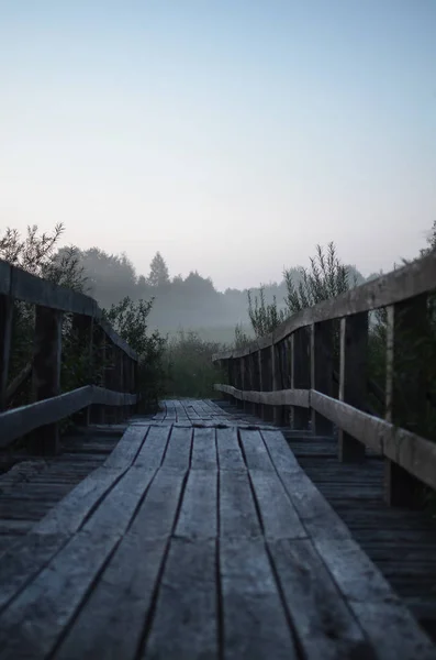 old wooden pedestrian bridge in thick morning fog - road in the distance