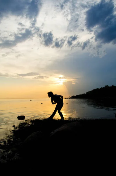 woman throws a stone into the water at sunset curving for a good throw