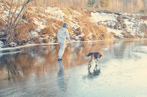 man walks with his dog on the first transparent winter ice, frozen on the surface of the river