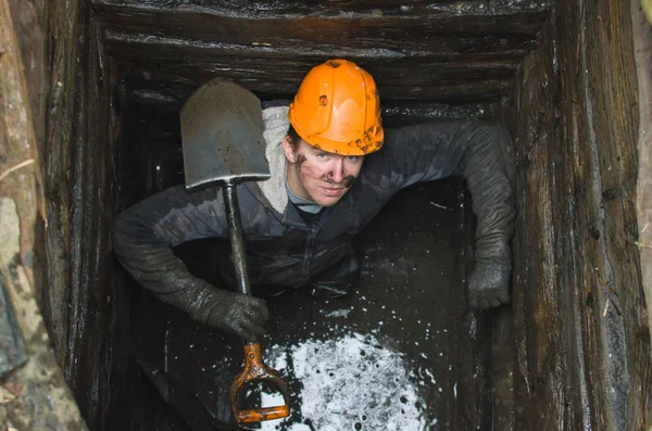 young worker in a construction helmet and a shovel cleans the old village well