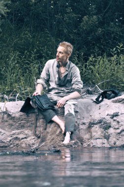 İkinci Dünya Savaşı ve kumlu sahilde oturan askeri bir çanta ile eski bir askeri üniforması giyen genç adam