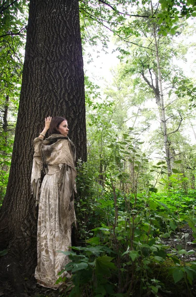年轻女子穿着一件旧的长裙 靠近一棵大树的树干 — 图库照片
