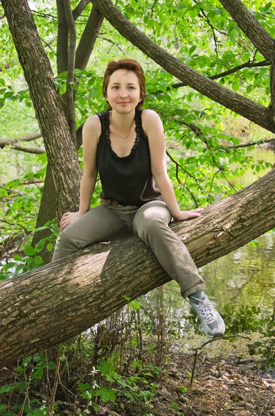 年轻女子休息在森林公园在夏天在一棵大树树干上 — 图库照片