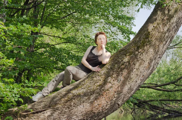 young woman resting in a forest Park in the summer on the trunk of a large tree