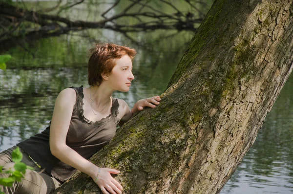 young woman resting in a forest Park in the summer on the trunk of a large tree