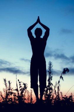 Gün batımında yoga pozunda duran bir adamın silüeti.