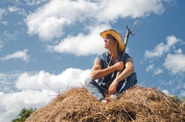 Ellerinde yaba olan genç bir adam samanlıkta oturup gökyüzüne bakıyor.