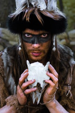 portrait of a young evil shaman with a skull of an animal in his hands close-up, he looks viciously, clearly wanting to curse all the animals, be afraid of him clipart