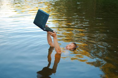 Adam gölde boğuluyor ama laptopunu kurtarmaya çalışıyor. Muhtemelen bir bilgisayar bağımlılığı.