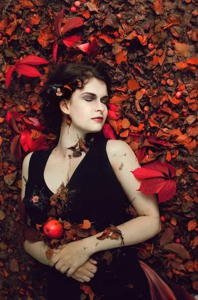美しい暗い髪の女性は古い庭の落ち葉の間に地面に横たわっていて秋を楽しんでいます — ストック写真