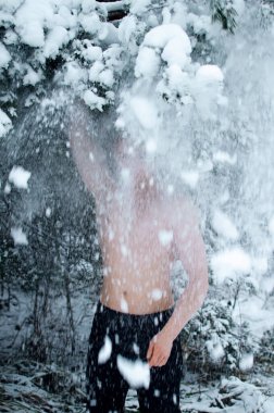 Genç adam kışın ormanda gömleksiz kar serpiyor.