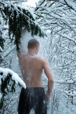 Genç adam kışın ormanda gömleksiz kar serpiyor.
