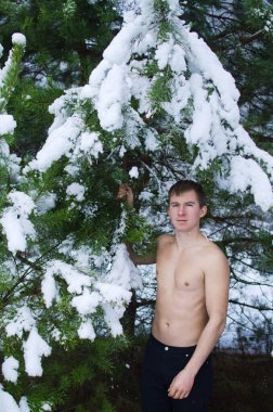 Genç adam kışın ormanda gömleksiz kar serpiyor.