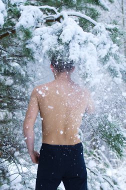Genç adam kışın ormanda gömleksiz kar serpiyor.