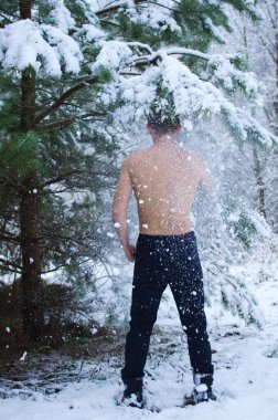 Genç adam kışın ormanda gömleksiz kar serpiyor.