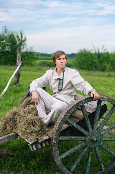 young man in national costume is sitting in an old cart in a field