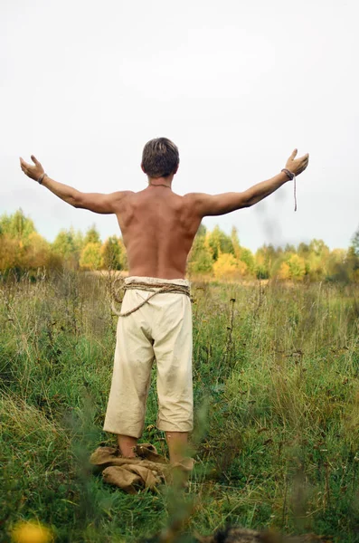腰にはぎ取られた若い男は腕を伸ばして野生の畑に立っている — ストック写真