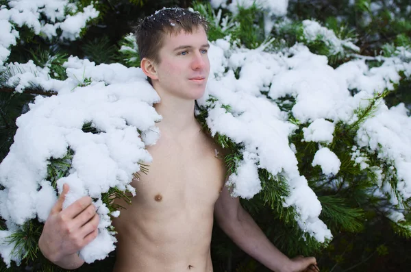 Genç adam kışın ormanda gömleksiz kar serpiyor.