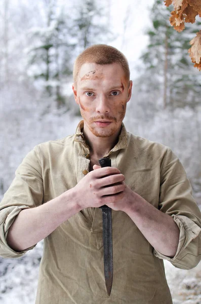 顔にあざのある若い兵士が冬の森の中にナイフを手に立ち — ストック写真