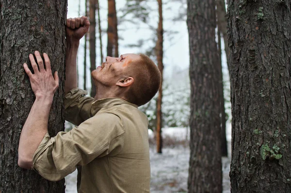在冬天的森林里 脸上沾满泥巴和伤痕的年轻士兵靠在松树树干上 图库图片