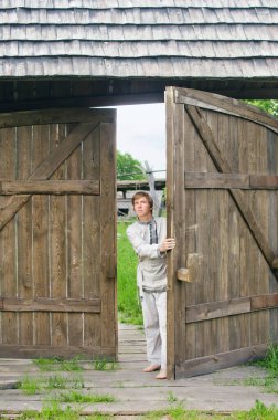 Eski elbiseli adam büyük bir ahşap kapı açıyor.