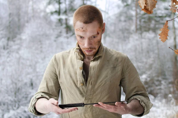 young man in a world war II military uniform with a combat cutlass in his hands in a snowy winter forest