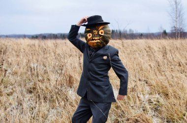 Kafasında Cadılar Bayramı balkabağı olan korkunç Korkuluk takım elbise giymiş vahşi bir tarlada duruyor.