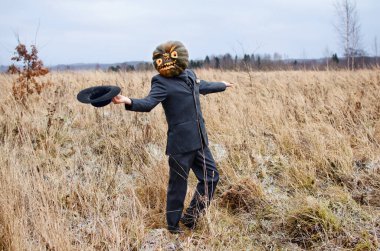 Kafasında Cadılar Bayramı balkabağı olan korkunç bir korkuluk iş elbisesi giymiş vahşi bir tarlada dans ediyor.