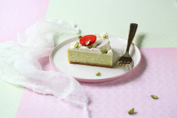 Piece of Pistachio Cheesecake with Vanilla Diplomat Cream, on light green and pink background.