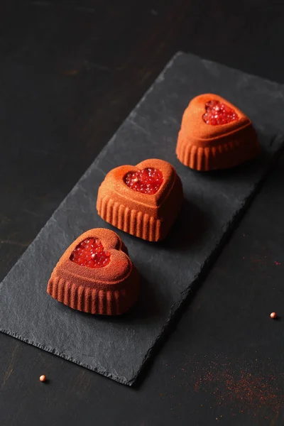 Çağdaş Çikolata Mini Mousse Kek kalp şeklinde silikon kalıp yapılmış, tuğla rengi kadife sprey ile kaplı ve kan portakal havyar ile dekore, siyah arka plan üzerinde.