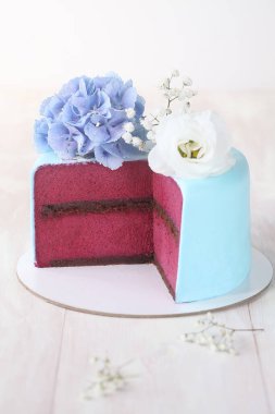 Glütensiz çikolatalı mini kek ve kuşüzümü köpüklü, açık mavi fondantla kaplanmış, taze çiçeklerle süslenmiş, gri tuğla bir arka planda..