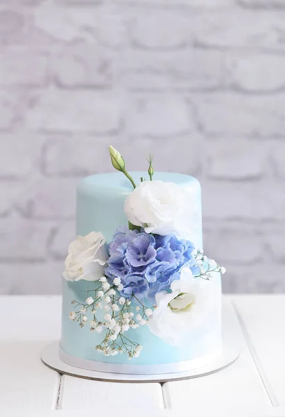 Two Tier Wedding Mini Cake decorated with fresh flowers, on a gray brick wall background.