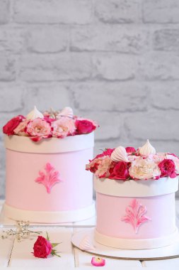 Açık pembe fondanla kaplanmış, açık gri tuğla bir duvar ve beyaz ahşap bir masa üzerinde pembe güllerle süslenmiş düğün çiçeği pastası..