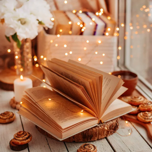 an open book with burning lights on a table by the window