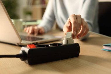 Geceleri evdeki bir masadaki dizüstü bilgisayarla elektrik prizinin prizini takan kadını kapat.