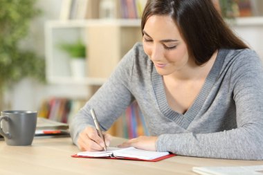 Mutlu kız ajandasına notlar yazıyor. Evdeki bir masada oturuyor.