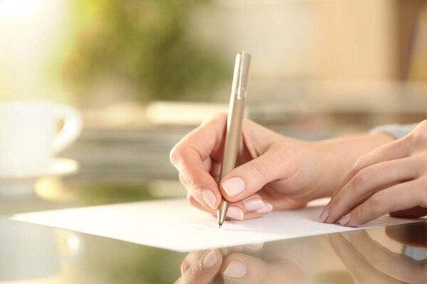 Close up of woman hand writing on a paper on a desk at home