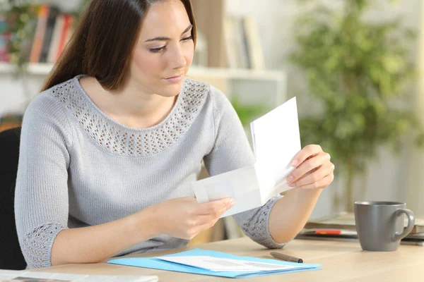 Serious woman opening envelope with letter inside sitting on a desk at home