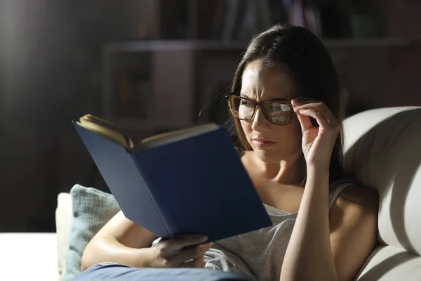 Gözlük takan kadın gece evde kitap okur.