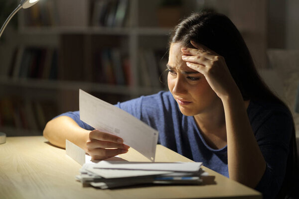 Worried woman looking at receipts at night sitting in the living room at home
