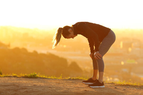 Side view portrait of a tired runner resting after exercise in city outskirts at sunset