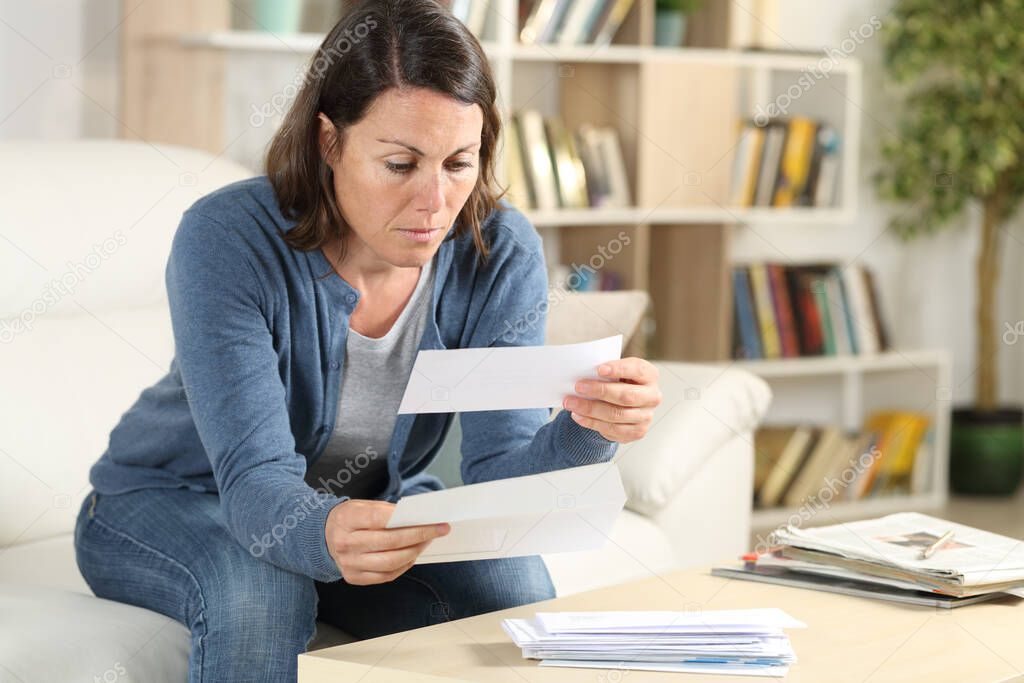 Serious adult woman looking at receipts letters sitting on the sofa at home
