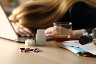 Close up of entrepreneur woman attempting suicide with pills and alcohol lying over desk at home office clipart