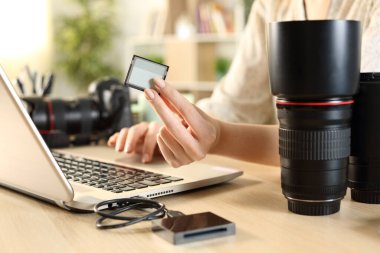 Evde dizüstü bilgisayar kullanarak hafıza kartı gösteren bir fotoğrafçı kadının ellerini kapat.