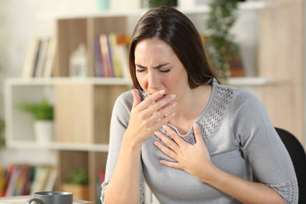 Sick woman coughing or wheezing sitting on a desk in the living room at home