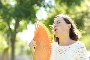 Yetişkin bir kadın yazın parkta dikilirken serinletici sıcak çarpması kullanıyor.